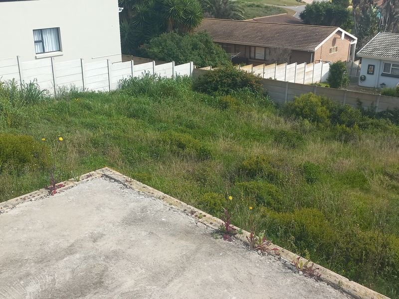 An elevated view of a vacant residential plot featuring a concrete slab foundation and surrounding precast boundary walls, currently covered in overgrown vegetation.