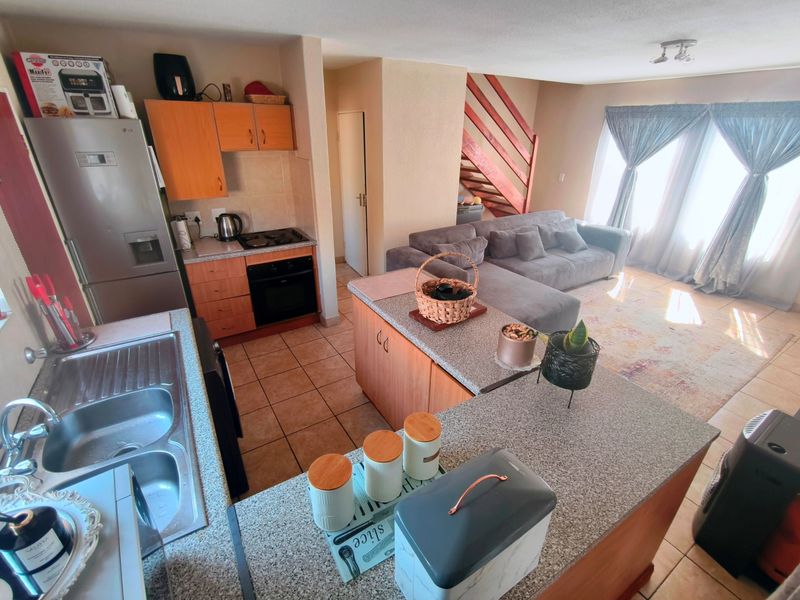 Open-plan living area featuring a functional kitchen with granite countertops, built-in oven, and hob, flowing into a comfortable lounge space with staircase access.