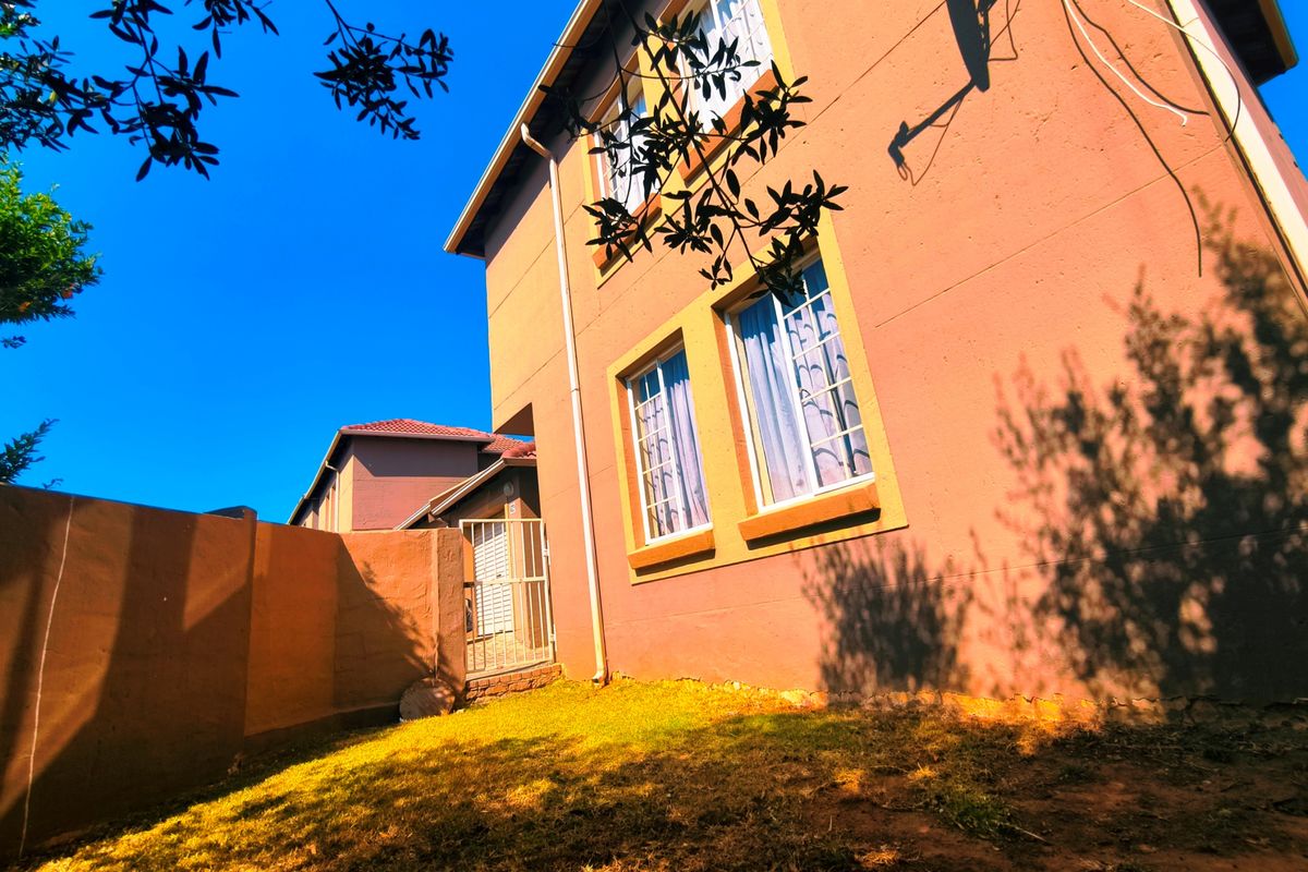 Rear exterior view of a multi-story townhouse featuring a small garden area, boundary wall, and security gate access.