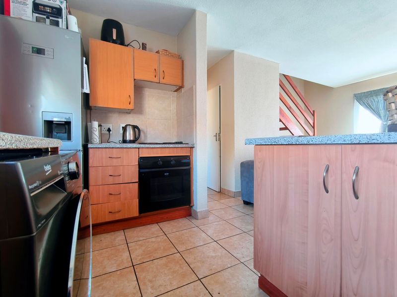 A functional kitchen featuring wood-finish cabinetry, laminate countertops, built-in oven and hob, with tiled flooring and an adjacent staircase.