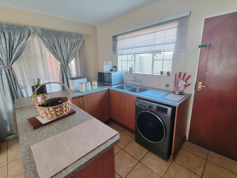 A functional kitchen featuring laminate cabinetry, granite-look countertops, a double bowl sink, and integrated laundry plumbing, with tiled flooring throughout.