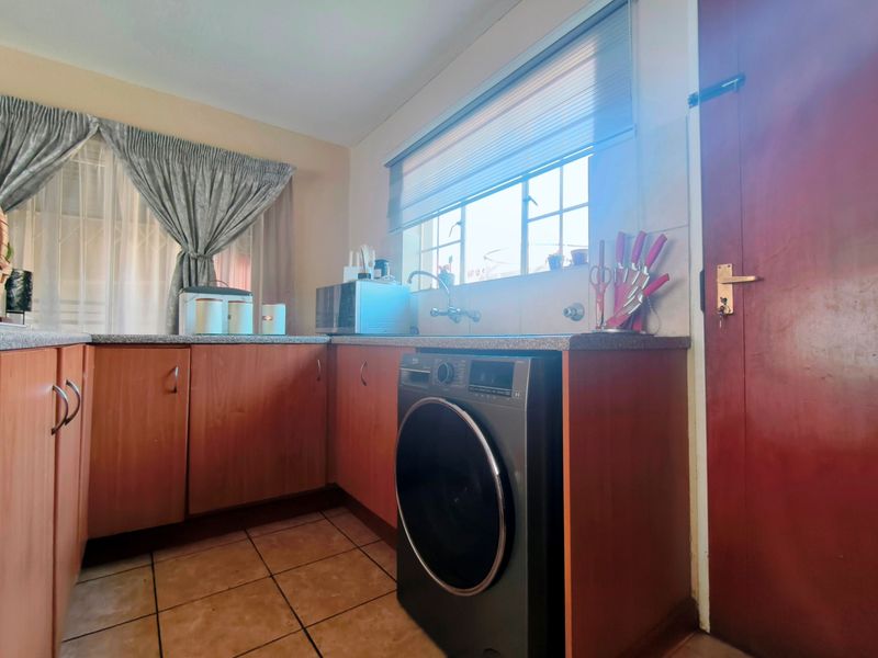A functional kitchen featuring wood-finish cabinetry, granite countertops, tiled flooring, and a dedicated space for a washing machine under the counter.