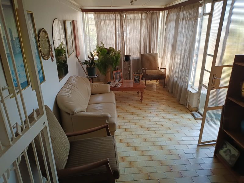 A sunlit living area featuring tiled flooring, large windows with curtains, and direct access through a glass panel door.