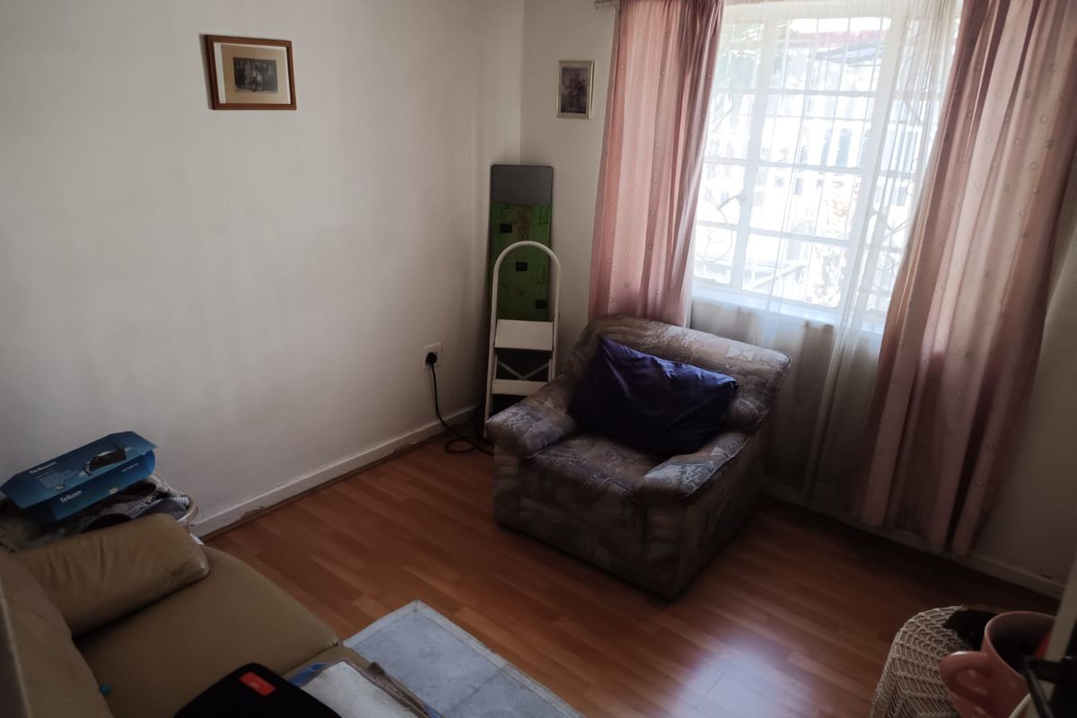 A bedroom featuring laminate flooring and a window fitted with security bars, offering a functional space with potential for cosmetic updates.
