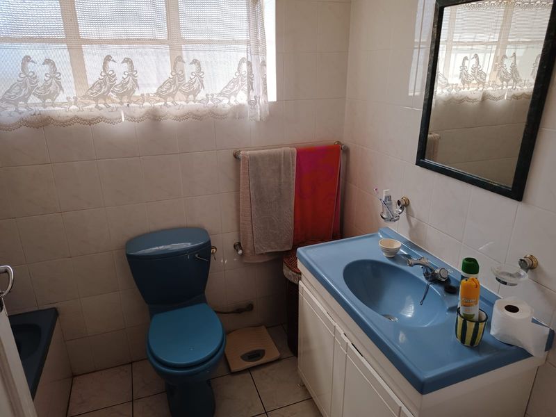 A functional bathroom featuring dated blue sanitaryware, tiled walls and flooring, and a wall-mounted mirror.