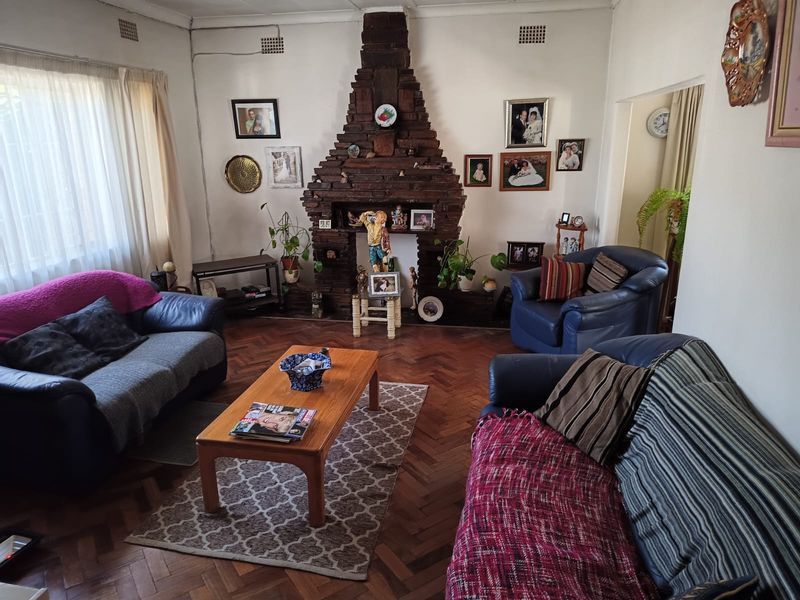A living room featuring a prominent brick fireplace and traditional parquet flooring, offering a classic layout with potential for modernization.