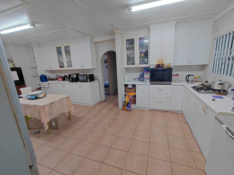 Spacious kitchen featuring white built-in cabinetry, gas hob, and tiled flooring. The space offers ample storage and potential for modernization.