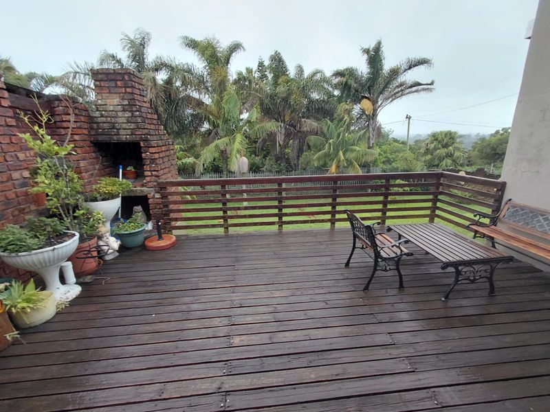 Outdoor timber deck featuring a built-in brick braai and wooden balustrade, overlooking a garden area.