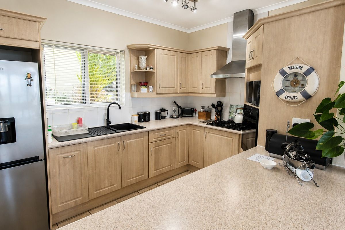 A functional kitchen featuring light wood-tone cabinetry, stone-look countertops, a gas hob with stainless steel extractor, and a modern black sink fixture.
