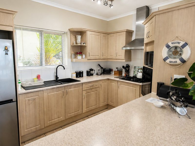 A functional kitchen featuring light wood-tone cabinetry, stone-look countertops, a gas hob with stainless steel extractor, and a modern black sink fixture.