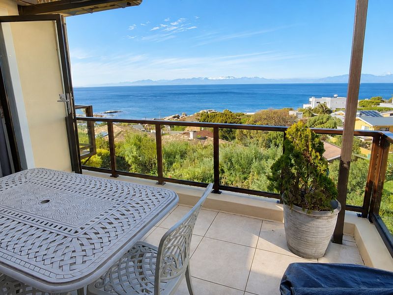A spacious balcony featuring tiled flooring and a glass balustrade, offering expansive ocean and coastal views.