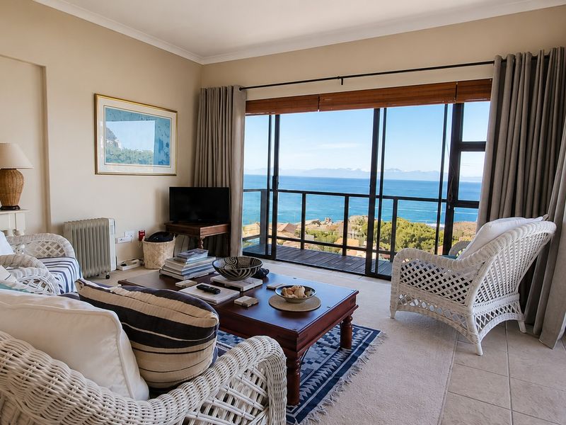 A bright living room featuring large sliding glass doors that open onto a balcony with expansive ocean and coastal views.