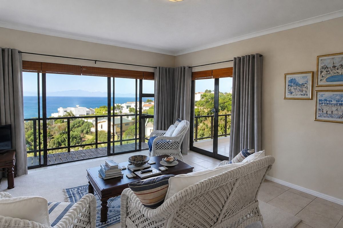 A bright living room featuring large sliding glass doors that open onto a balcony, offering expansive coastal and landscape views.
