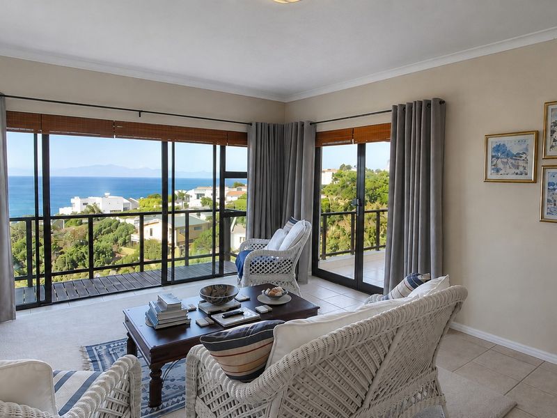 A bright living room featuring large sliding glass doors that open onto a balcony, offering expansive coastal and landscape views.