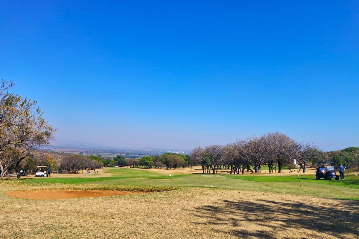 A scenic view overlooking a well-maintained golf course with mature trees and a sand bunker under a clear blue sky.