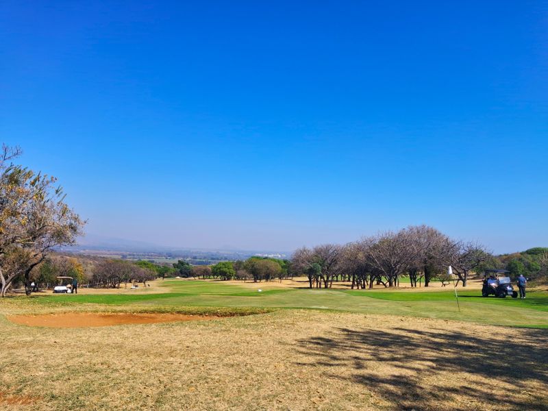 A scenic view overlooking a well-maintained golf course with mature trees and a sand bunker under a clear blue sky.