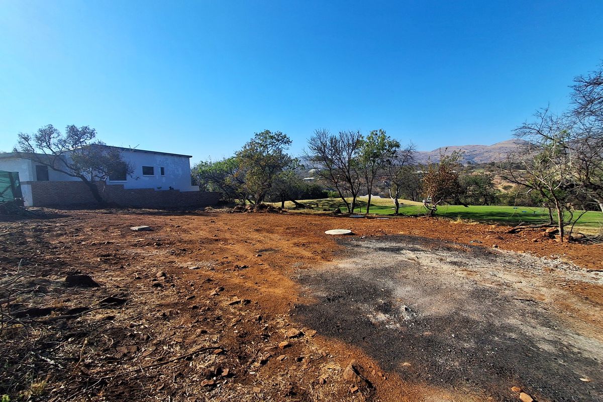 A vacant residential plot featuring cleared earth, a retaining wall, and distant landscape views, ready for development.