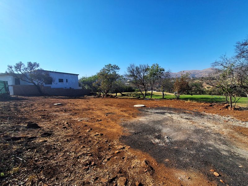 A vacant residential plot featuring cleared earth, a retaining wall, and distant landscape views, ready for development.