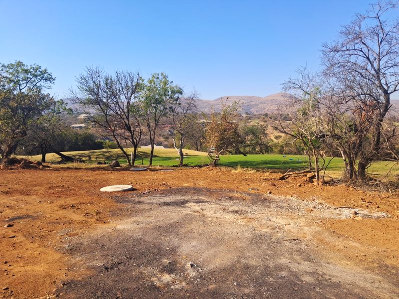 A view of a vacant residential plot overlooking a golf course and distant hills, featuring natural vegetation and clear site access.