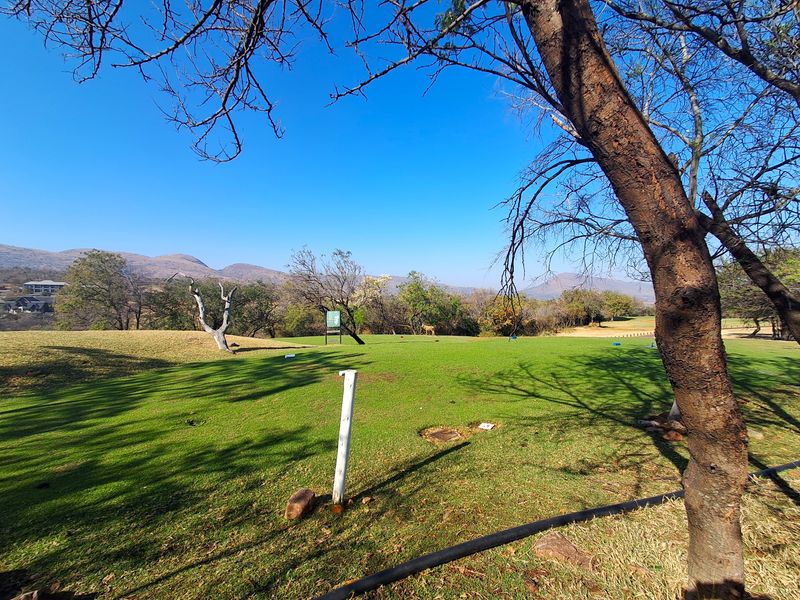 A scenic view of a well-maintained residential plot featuring expansive green lawns, mature trees, and a picturesque mountain landscape in the background.