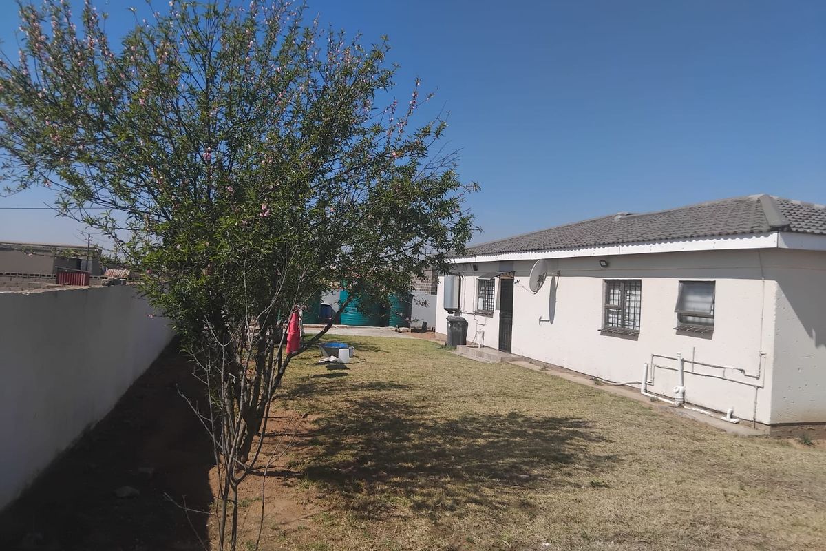 Rear view of the property featuring a lawn, boundary wall, and exterior wall with security bars on windows.