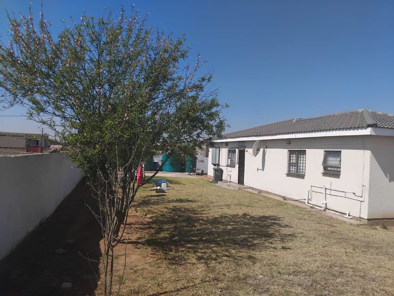 Rear view of the property featuring a lawn, boundary wall, and exterior wall with security bars on windows.