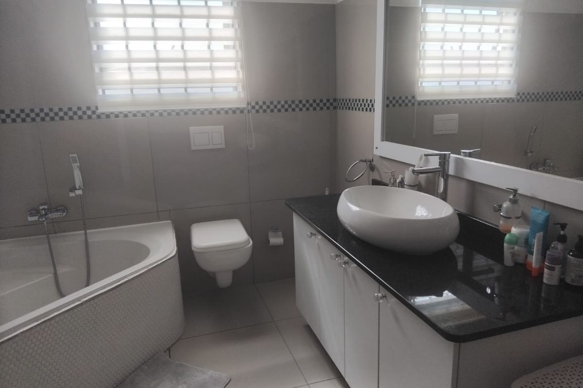 Modern bathroom featuring a corner bathtub, wall-mounted toilet, and a vanity with a vessel sink and granite countertop.