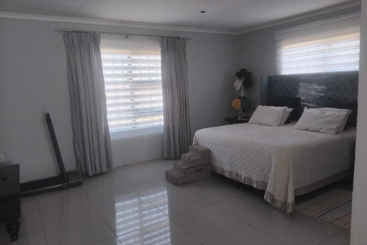Spacious bedroom featuring neutral wall tones, large windows with fitted blinds and curtains, and polished tiled flooring throughout.