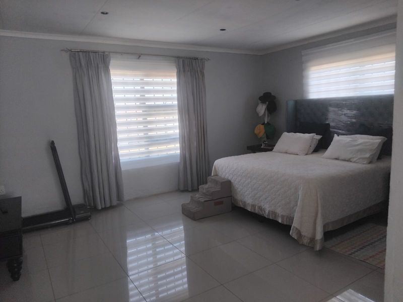 Spacious bedroom featuring neutral wall tones, large windows with fitted blinds and curtains, and polished tiled flooring throughout.