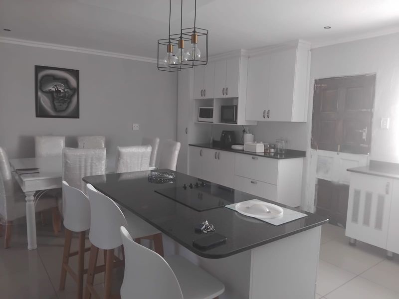 Modern open-plan kitchen and dining area featuring a central island with a built-in hob, white cabinetry, and sleek tiled flooring.