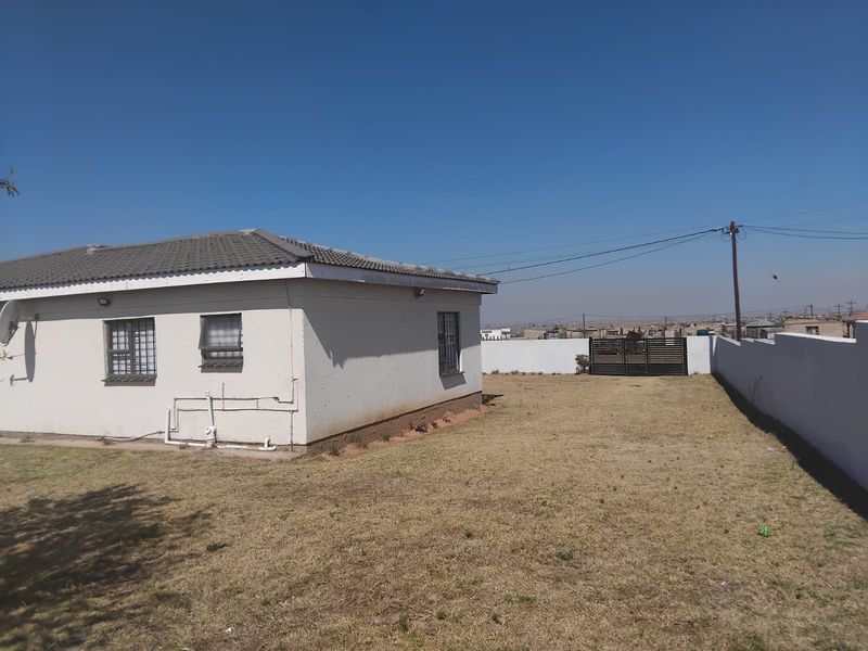 Rear view of the property featuring a tiled roof, security bars on windows, and a large enclosed garden with a boundary wall and metal gate.