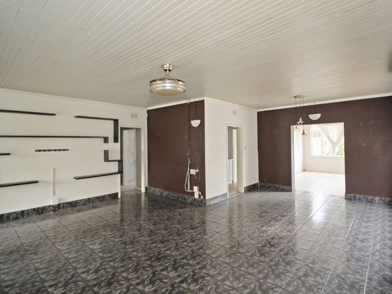 Spacious living area featuring tiled flooring, tongue and groove ceiling, and built-in wall shelving, offering a blank canvas for interior design.