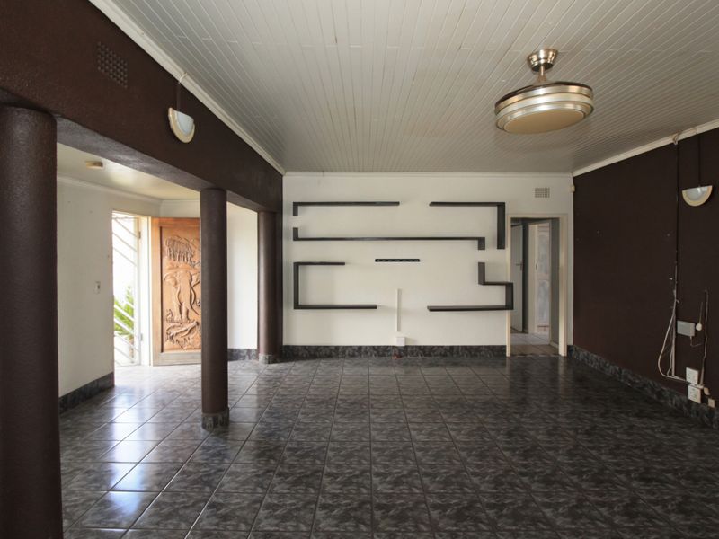 Spacious living area featuring dark tiled flooring, built-in wall shelving, structural columns, and a unique carved wooden entrance door.