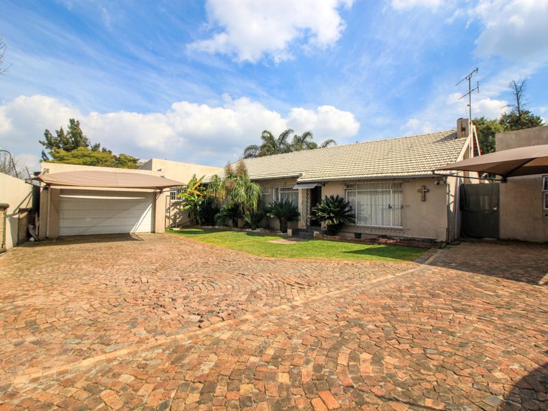 Front exterior view of a single-story house featuring a large brick-paved driveway, a garage, and a carport.
