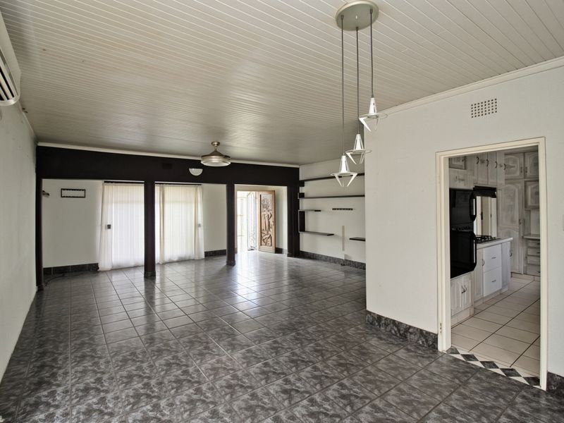 Spacious open-plan living area featuring tiled flooring, timber panelled ceilings, built-in shelving, and direct access to the kitchen.