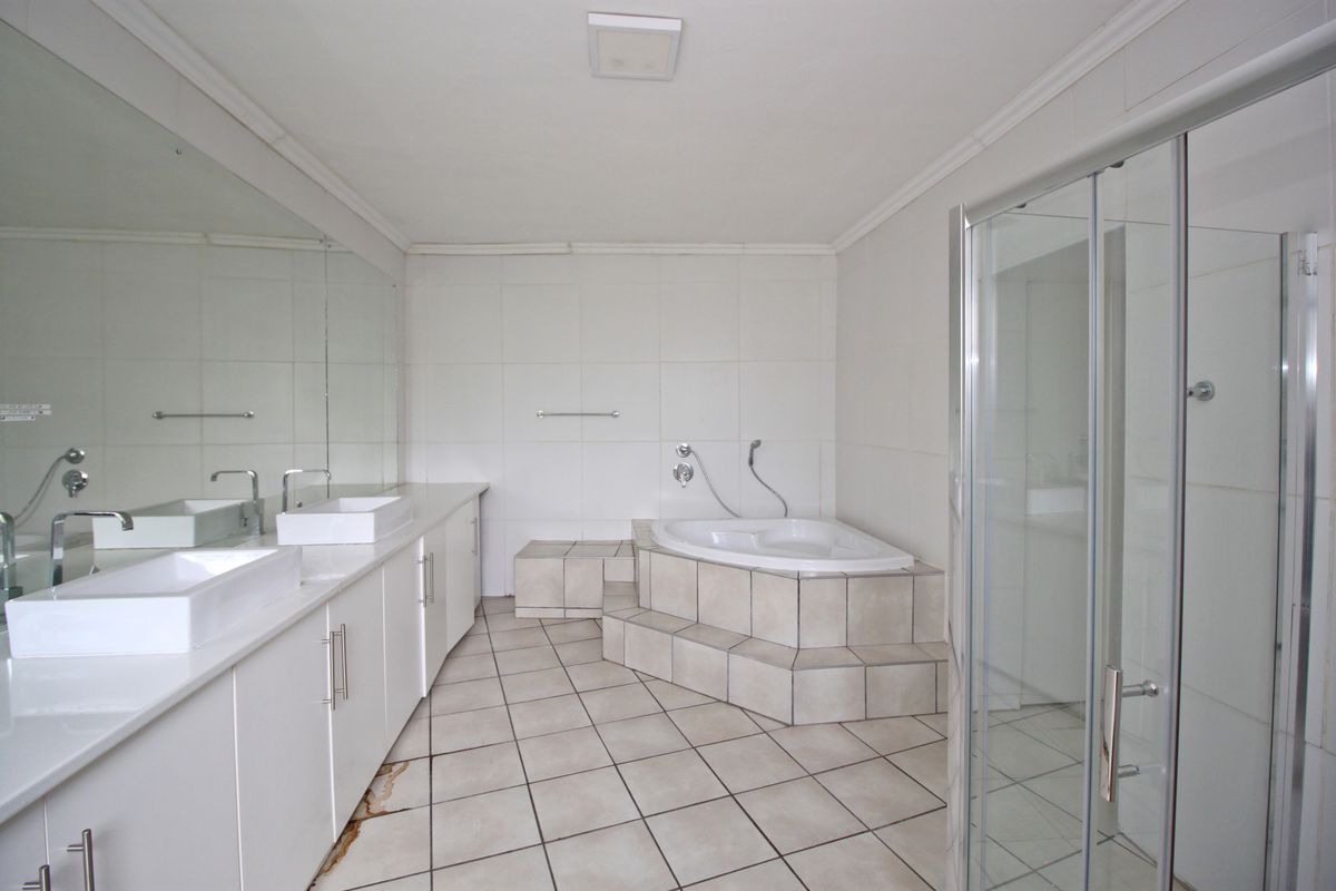 Spacious bathroom featuring a double vanity, built-in corner bathtub, and a separate glass-enclosed shower with neutral tiled finishes.
