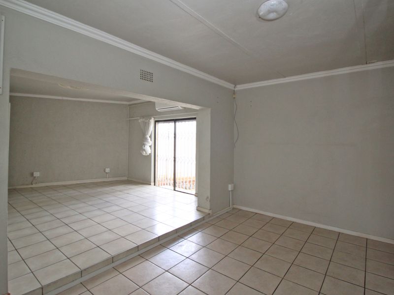 An empty, open-plan living area featuring tiled flooring, a raised section, and a sliding glass door leading to an outdoor space.