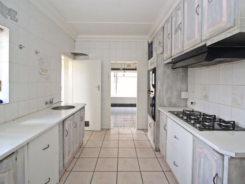 A galley-style kitchen featuring built-in cabinetry, a gas hob, an extractor fan, and an integrated oven, with tiled flooring and wall finishes throughout.