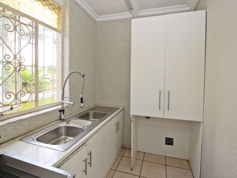 A functional scullery area featuring a double stainless steel sink, built-in cabinetry, and tiled flooring, offering practical space for laundry or kitchen preparation.
