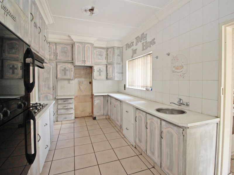 A functional kitchen featuring tiled flooring, built-in cabinetry, a gas hob, and an integrated oven, offering a blank canvas for modern renovation.