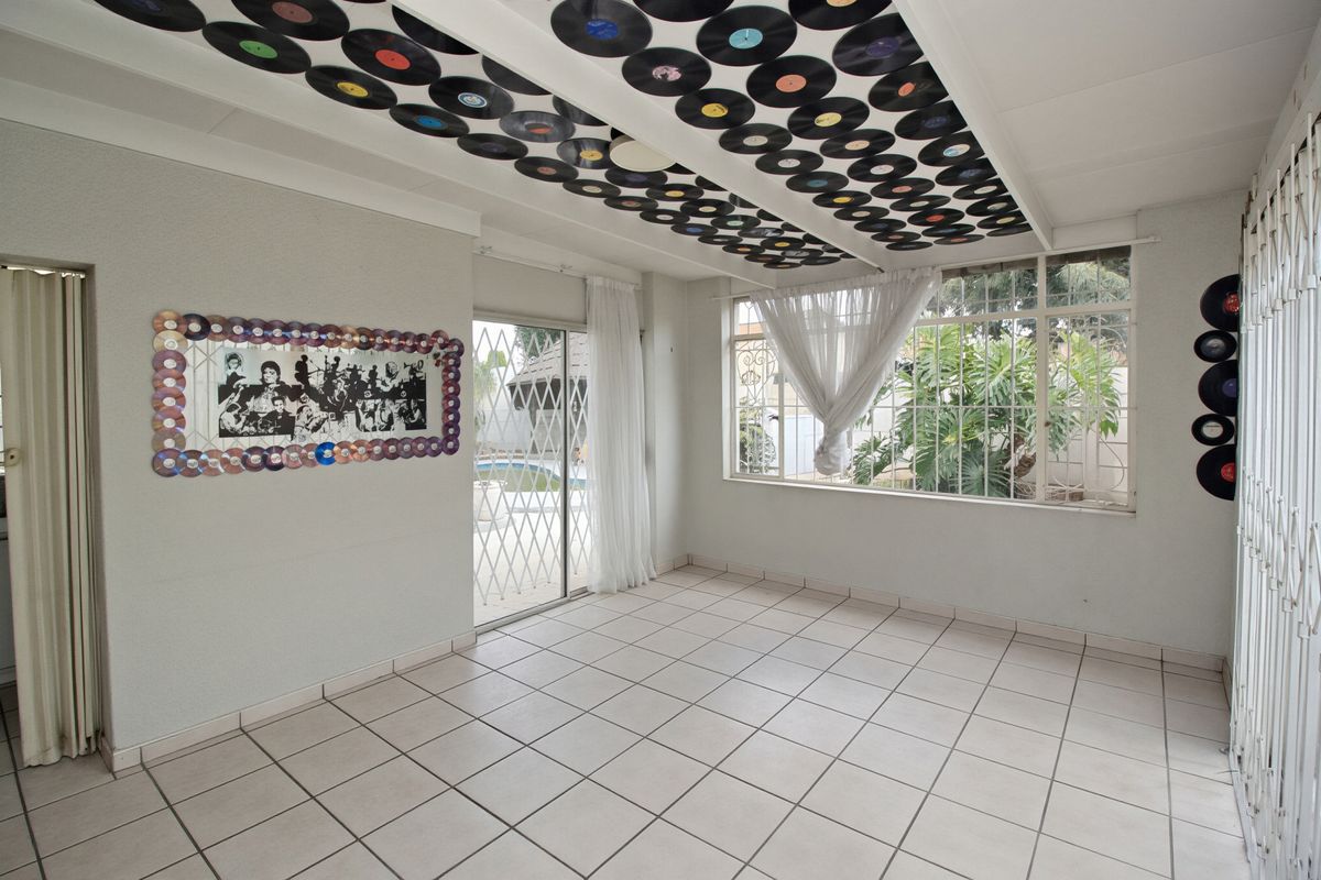 An empty living room featuring tiled flooring, large windows, and a sliding glass door with security gates leading to the outdoor area.