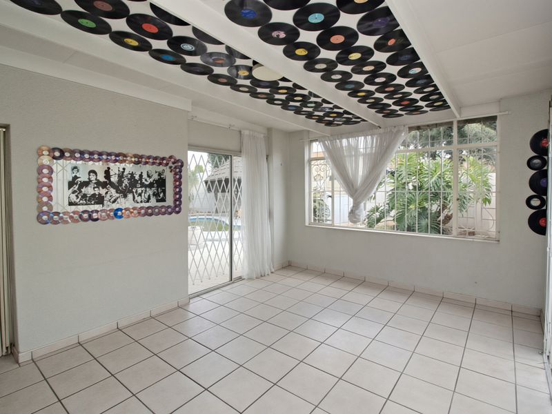 An empty living room featuring tiled flooring, large windows, and a sliding glass door with security gates leading to the outdoor area.
