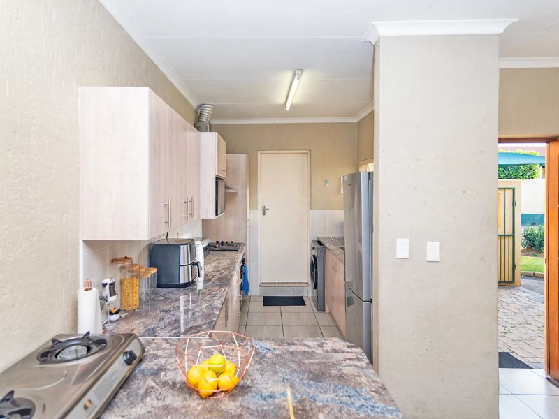 A functional kitchen featuring laminate cabinetry, stone-look countertops, built-in hob, and tiled flooring with direct access to the exterior.