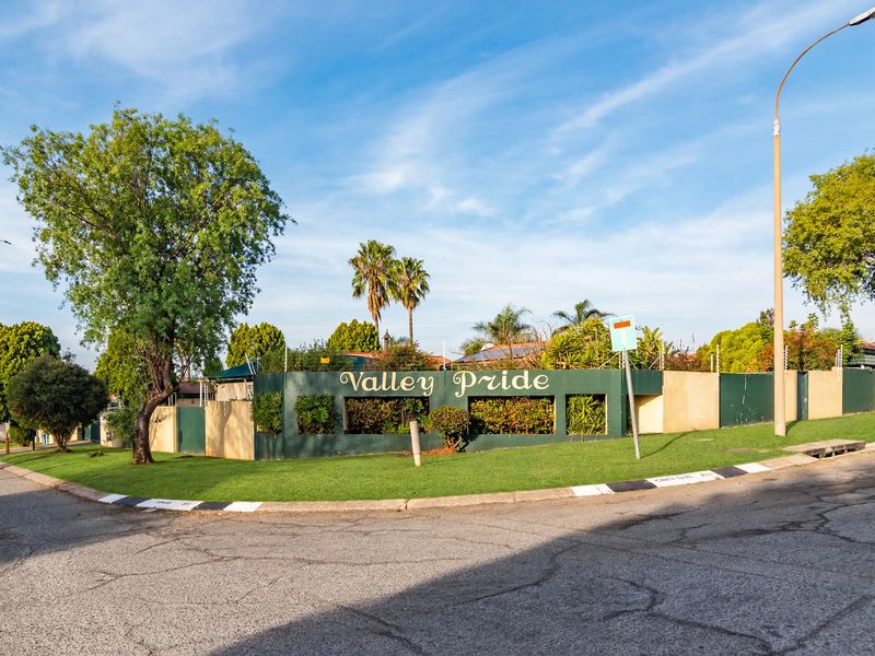 Street view of the Valley Pride townhouse complex entrance, featuring a landscaped perimeter wall and security fencing.
