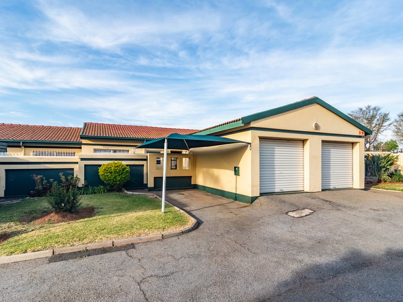 Front exterior view of a townhouse featuring a double garage with roller doors, a shade cloth carport, and a paved driveway.