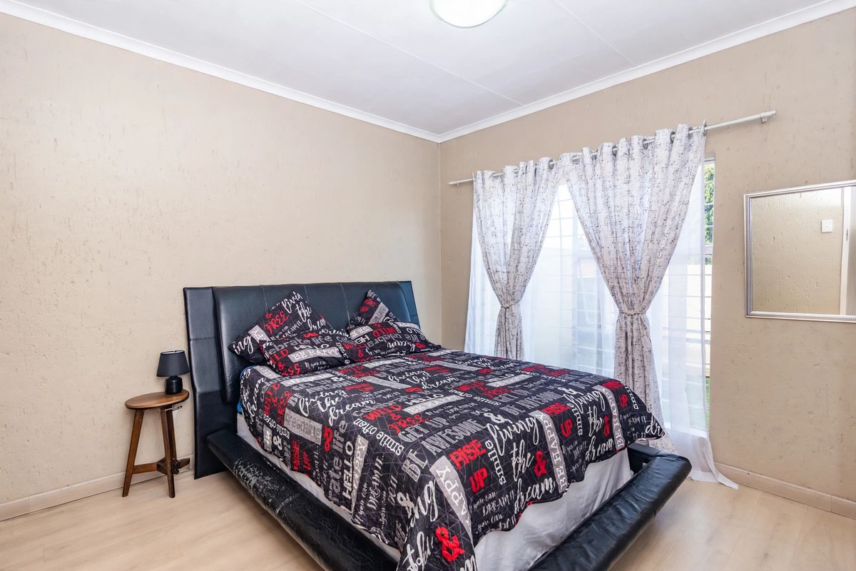 A bedroom featuring light-toned laminate flooring, coved ceilings, and a window fitted with security bars.