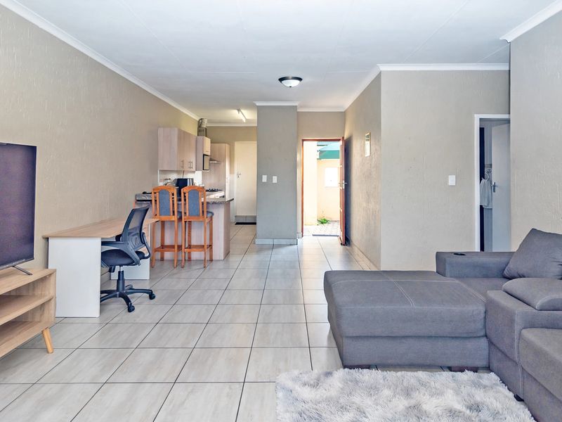 Open-plan living area featuring tiled flooring, a functional kitchen with breakfast counter, and direct access to an exterior doorway.