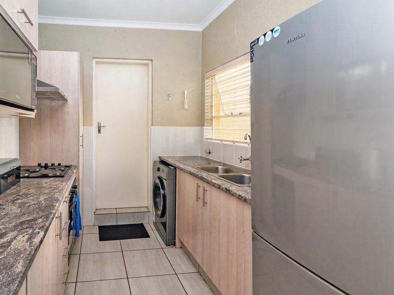 Functional kitchen featuring light wood cabinetry, granite-look laminate countertops, a gas hob with extractor, and tiled flooring with direct access to an exterior door.