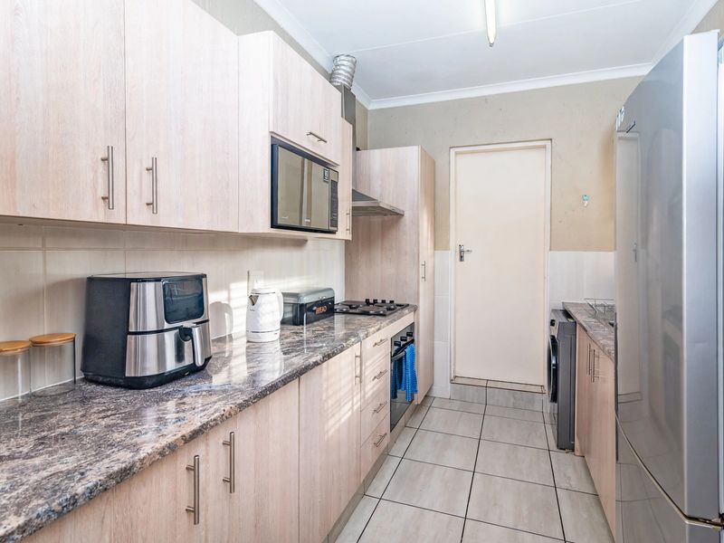 A functional kitchen featuring light wood-finish cabinetry, granite countertops, a built-in oven, gas hob, and tiled flooring with a neutral backsplash.