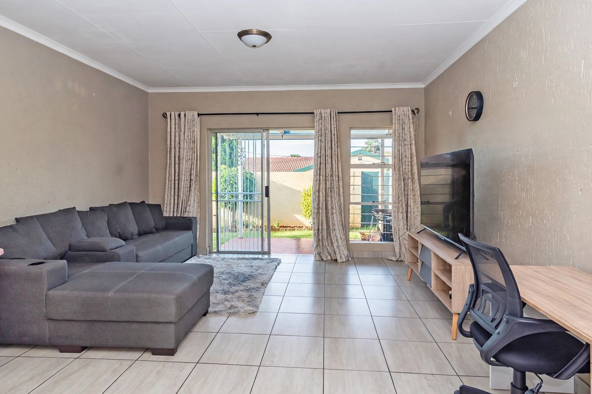 A bright living room featuring tiled flooring, a sliding glass door with security gate, and direct access to the rear patio area.